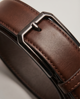 Nahaufnahme des braunen Ledergürtels mit silberner Metallschnalle – elegante Details im Fokus.