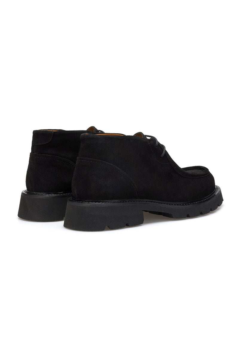 Boots displayed on a wooden floor, highlighting their sleek silhouette.